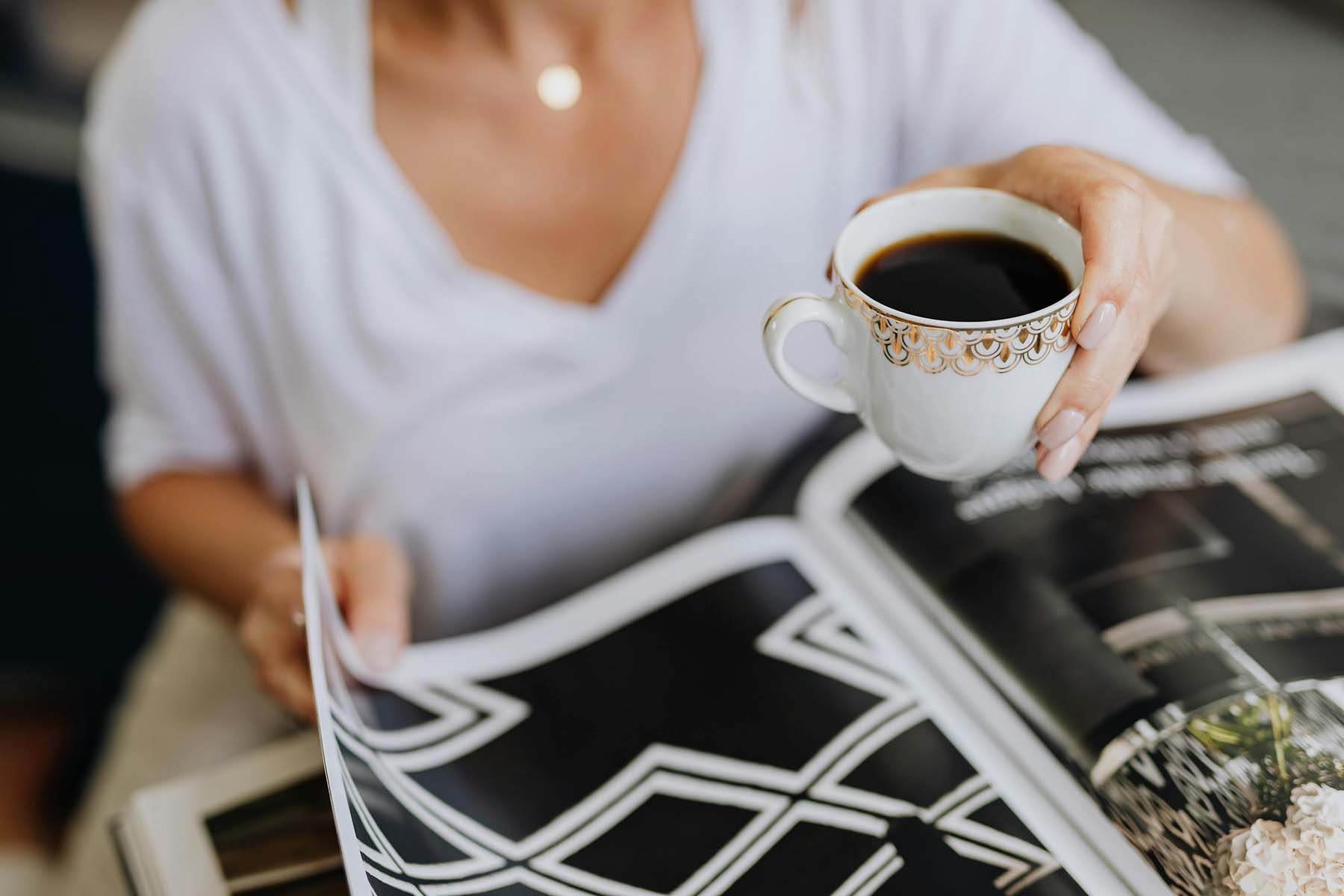 Woman holding a cup of coffee while reading a magazine