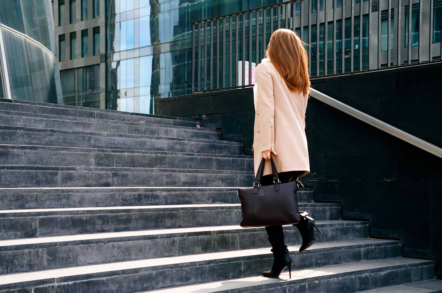 Businesswoman walking up outdoor stairs with a black handbag