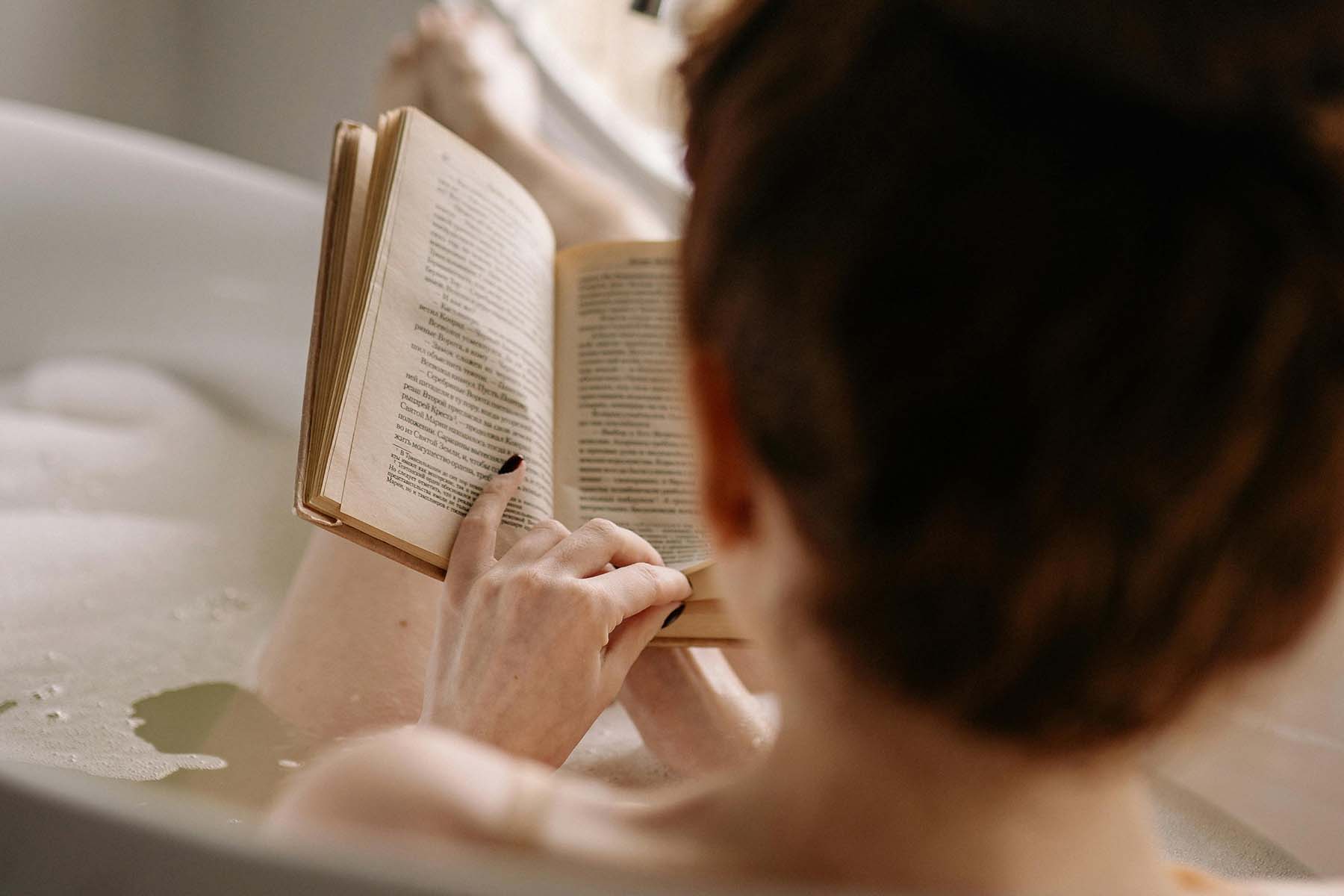 Person reading a book while relaxing in a bathtub