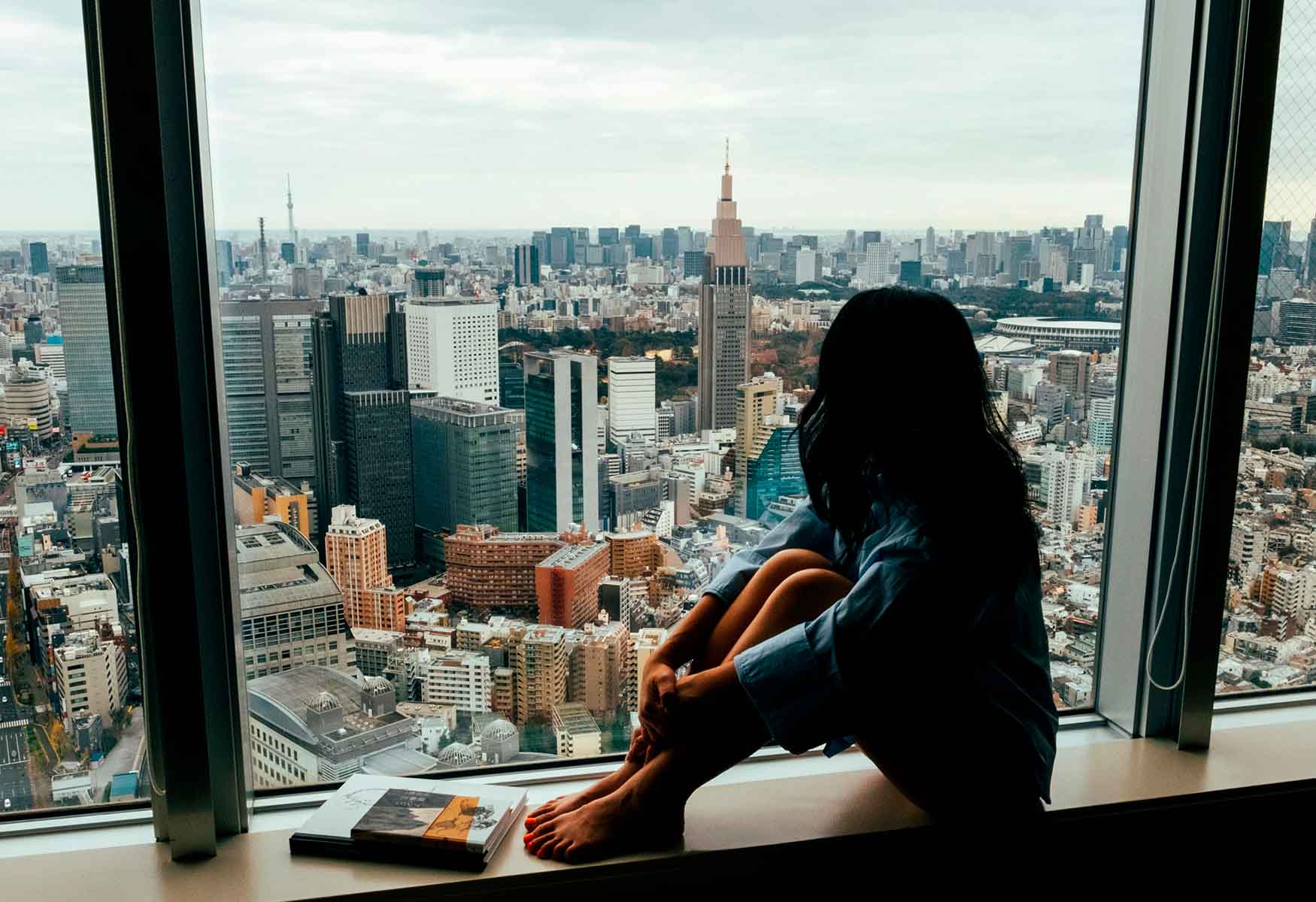 Woman sitting by a large window overlooking a city skyline